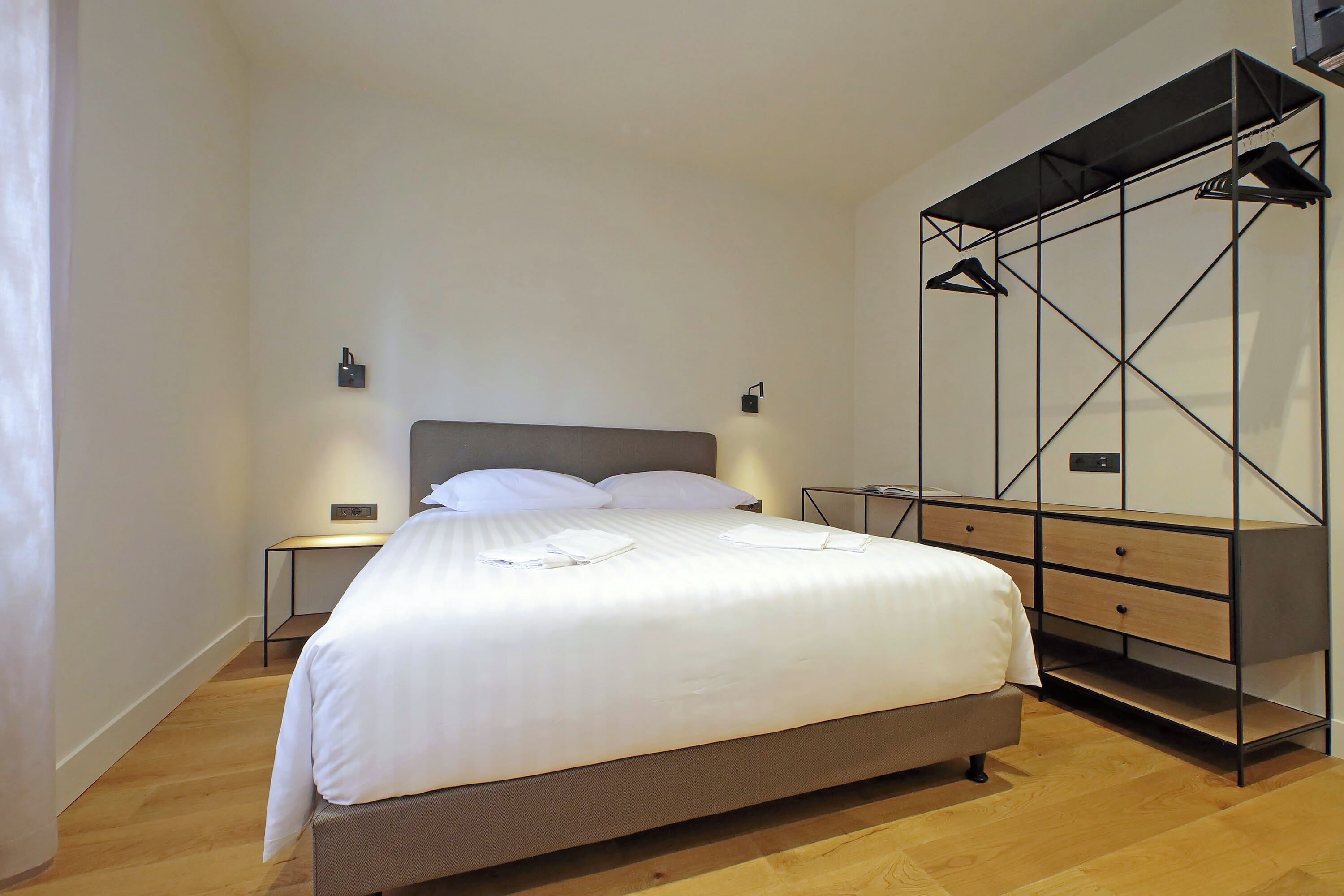 A modern bedroom with a large bed, a wooden dresser, and a built-in wardrobe with hanging space.