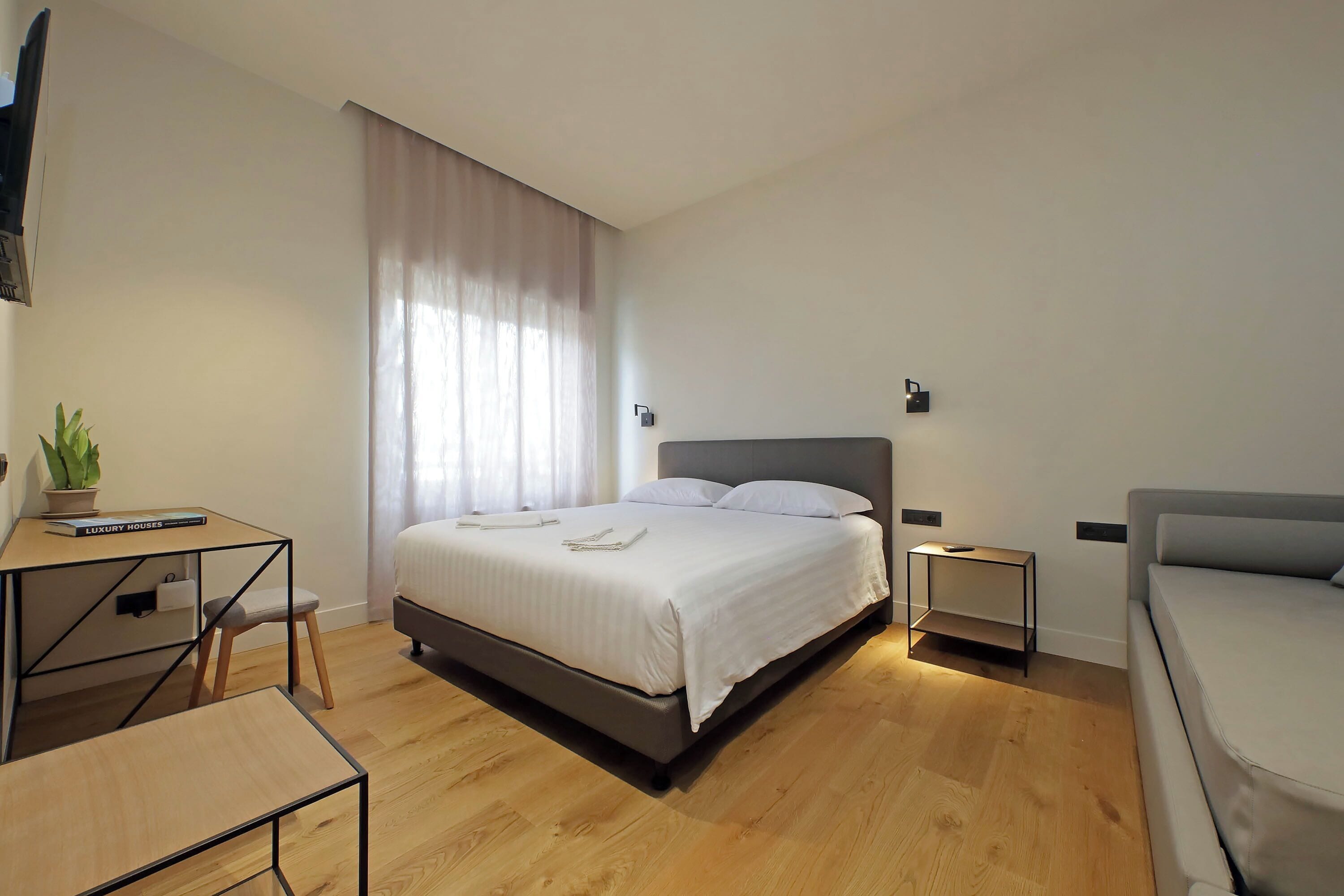 A modern bedroom with a bed, bedside tables, a desk, and a chair.