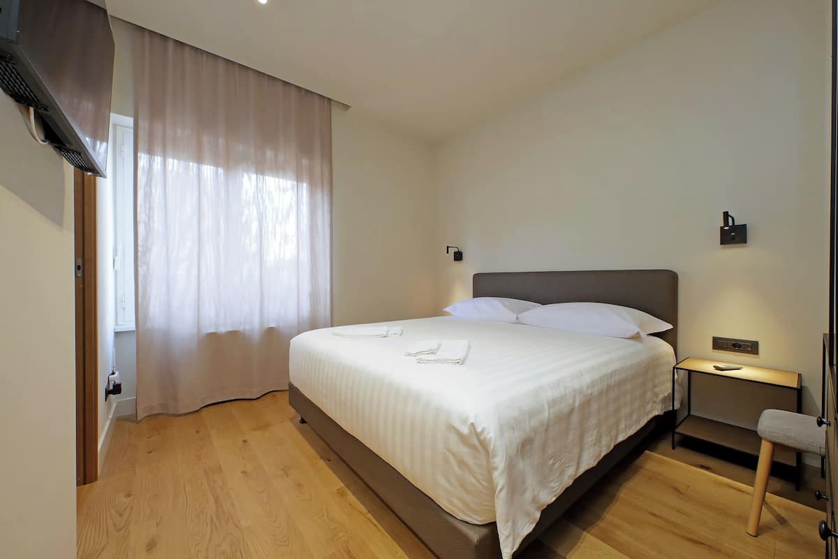 A neatly made bed with white linens, a bedside table with a lamp, and a wooden floor.