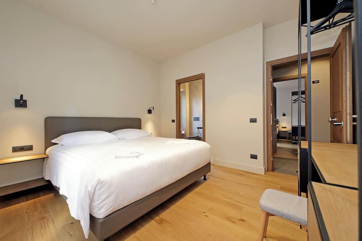 A modern bedroom with a large bed, bedside tables, a bench, and a mirror.