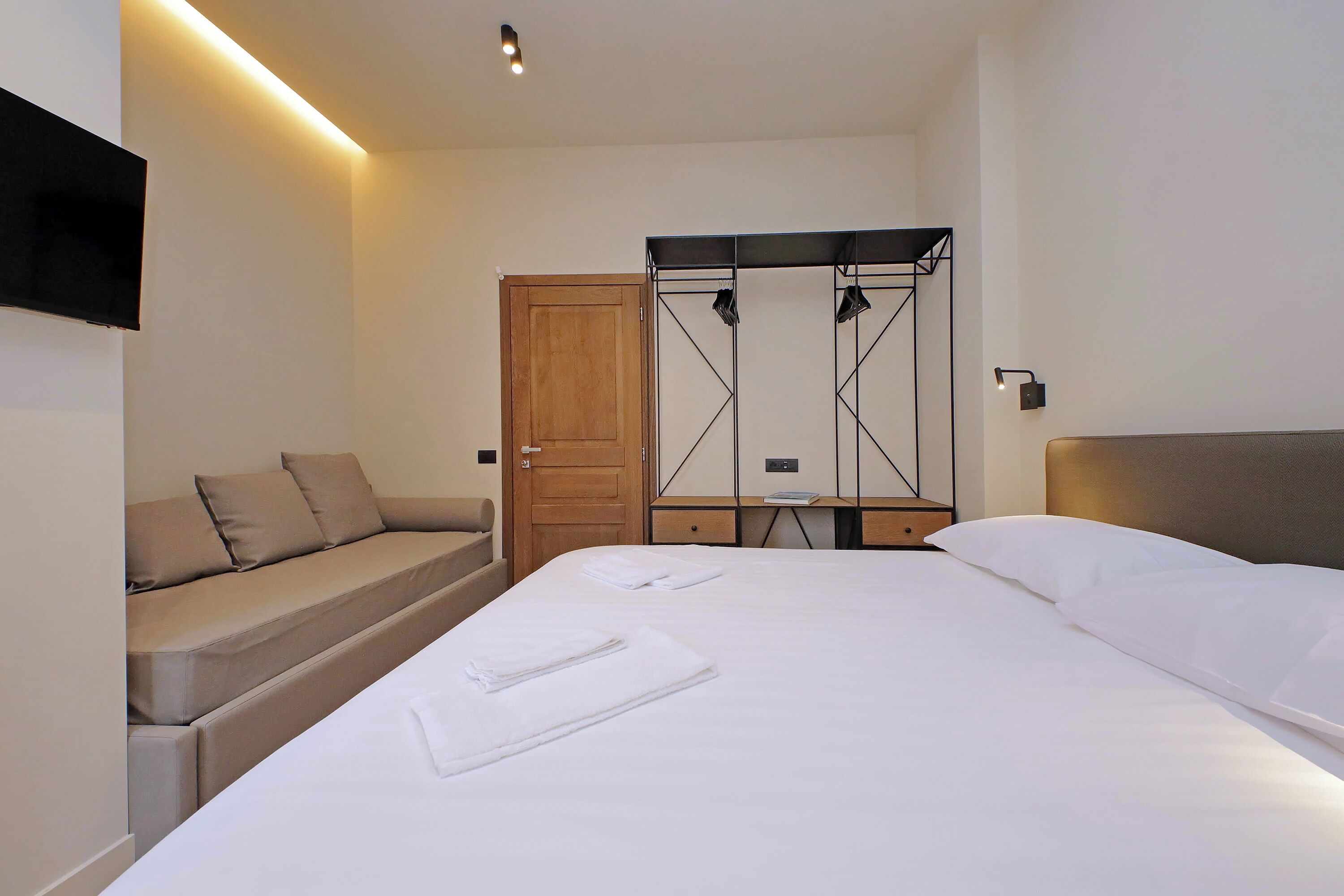 Una camera d'albergo con un letto, un divano, un armadio e una TV a parete.