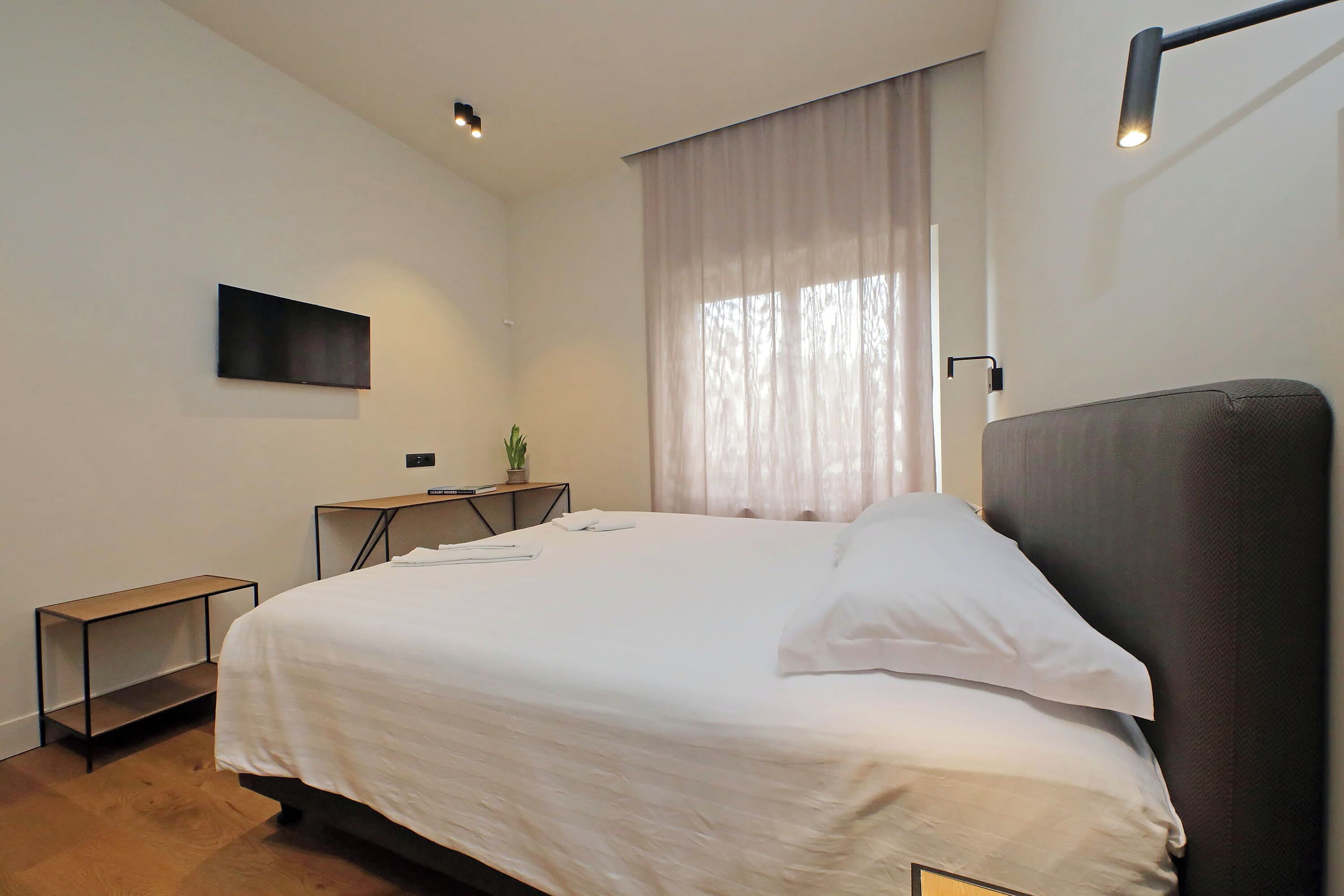 A modern bedroom with a large bed, a desk, and a TV mounted on the wall.