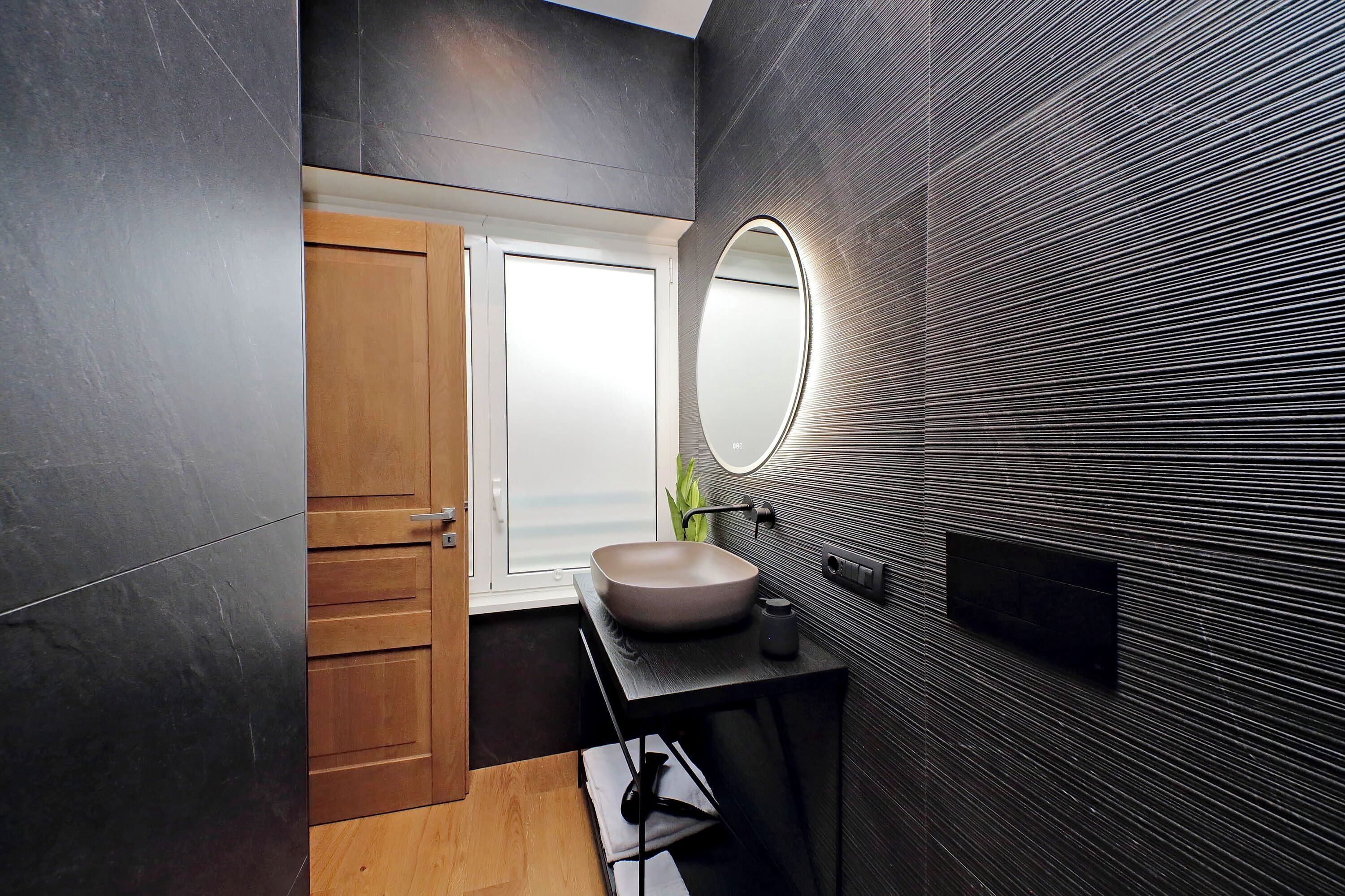 A modern bathroom with a wooden door, a round mirror, and a beige sink.