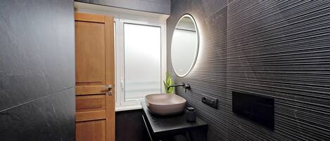 A modern bathroom with a wooden door, a round mirror, and a beige sink.