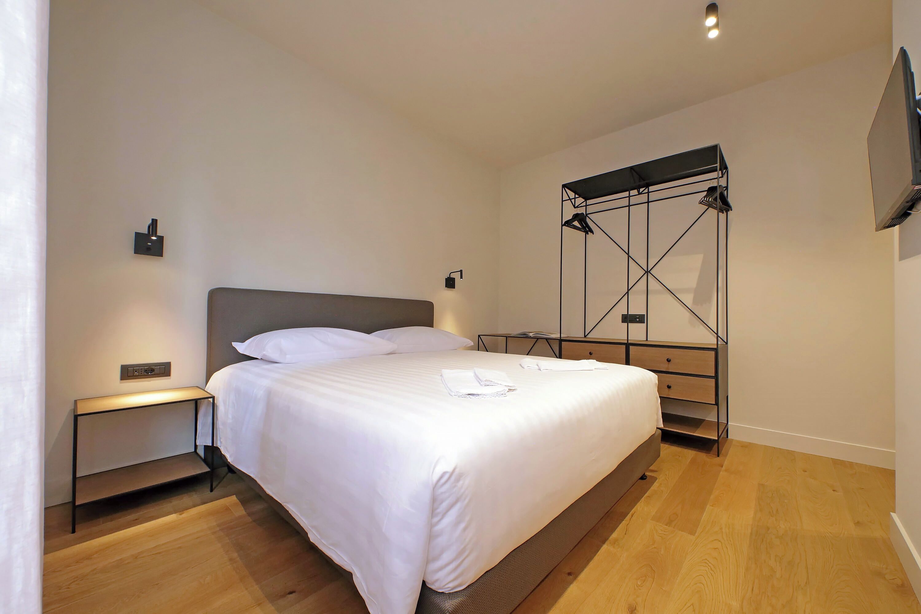 A neatly made bed with white linens, a bedside table with a lamp, and a wall-mounted TV.