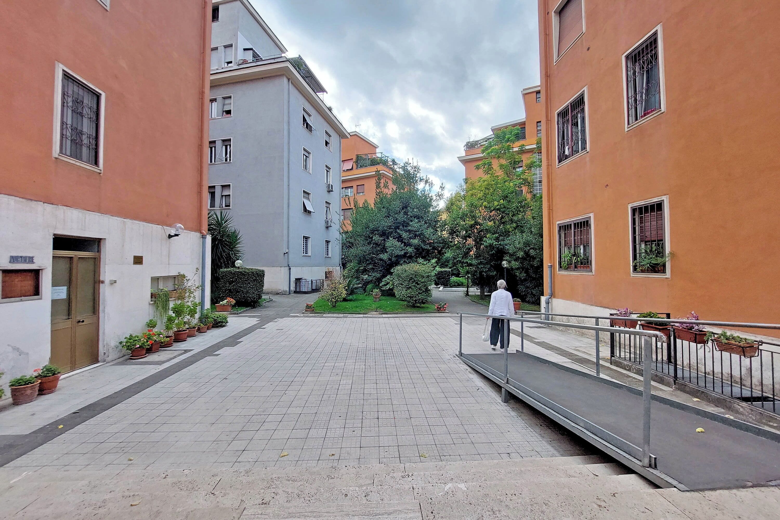 A courtyard with potted plants, a pedestrian pathway, and buildings with balconies.