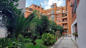 A courtyard with a pathway, surrounded by orange buildings with balconies, and various potted plants. - The Place Gallia (Rome)