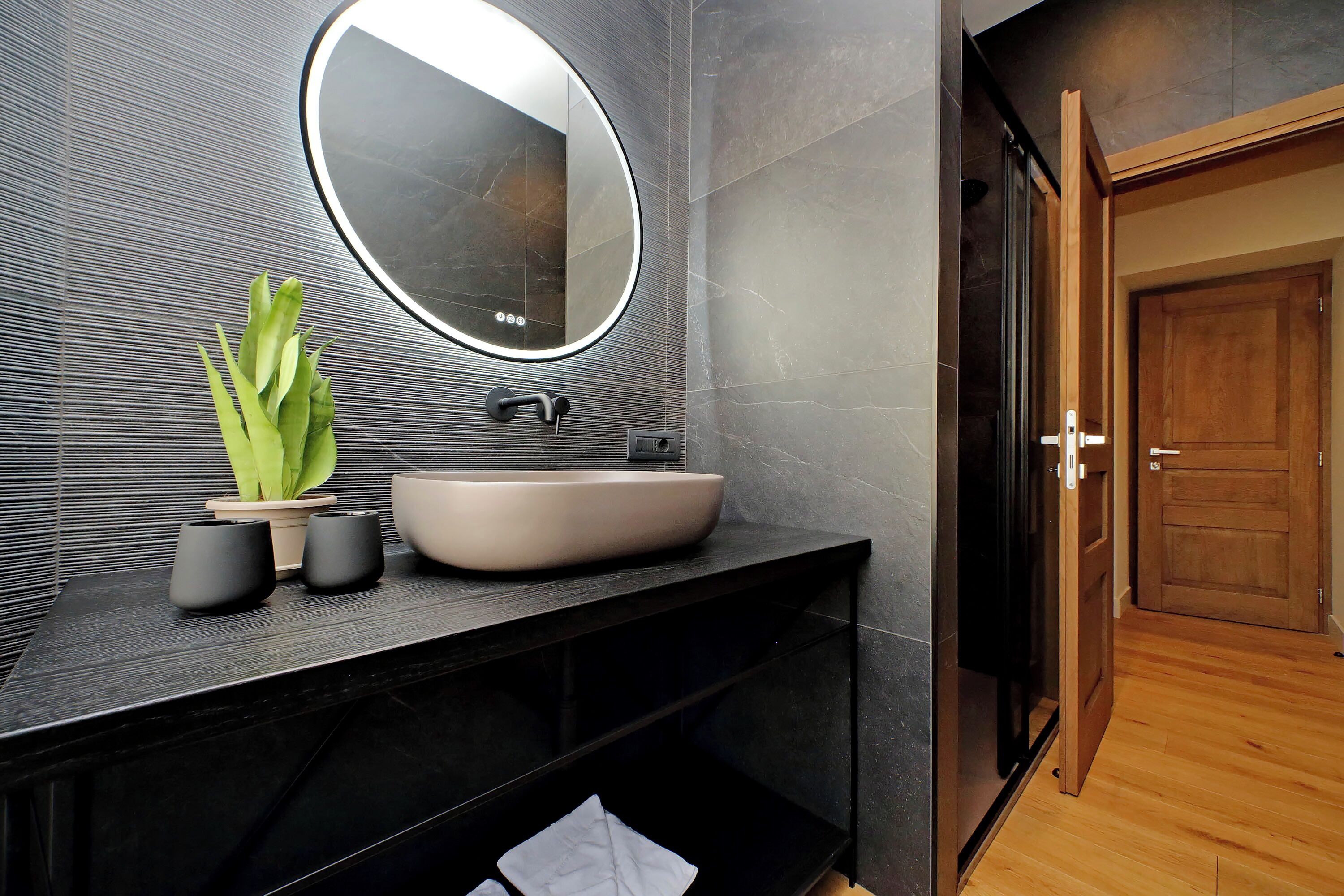 A modern bathroom with a large round mirror, a vessel sink, and a potted plant.