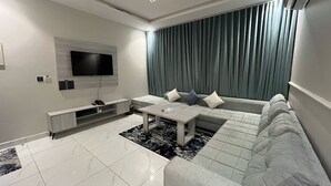 A modern living room with a sectional sofa, a coffee table, a flat-screen TV, and a wall-mounted entertainment unit. - luluat alsafa apatments (Jeddah)