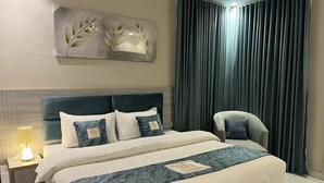 A modern hotel room with a large bed, a headboard, a nightstand with a lamp, a chair, and a painting on the wall. - luluat alsafa apatments (Jeddah)