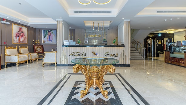 A reception area with a glass-top table, gold chairs, and a modern chandelier. - luluat alsafa apatments (Jeddah)