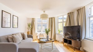 Ein modernes Wohnzimmer mit einer Couch, einem Sessel, einem Fernseher und Zierpflanzen.