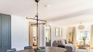 Ein modernes Wohnzimmer mit Essbereich, ausgestattet mit einem Holztisch, einem grauen Sofa und einer Pendelleuchte.