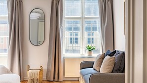 Ein modernes Wohnzimmer mit einem grauen Sofa, einem runden Spiegel und einem Fenster mit Vorhängen.