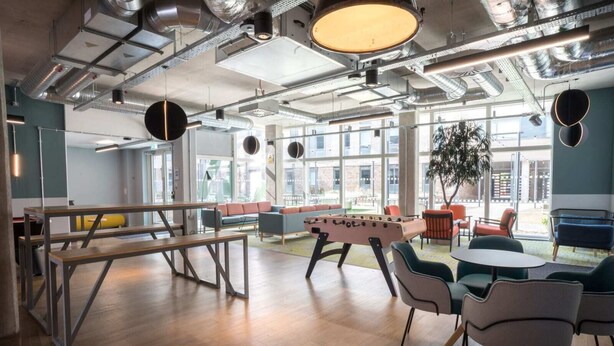 Un espace intérieur moderne doté d’un baby-foot, d’un coin salon et de grandes fenêtres.
