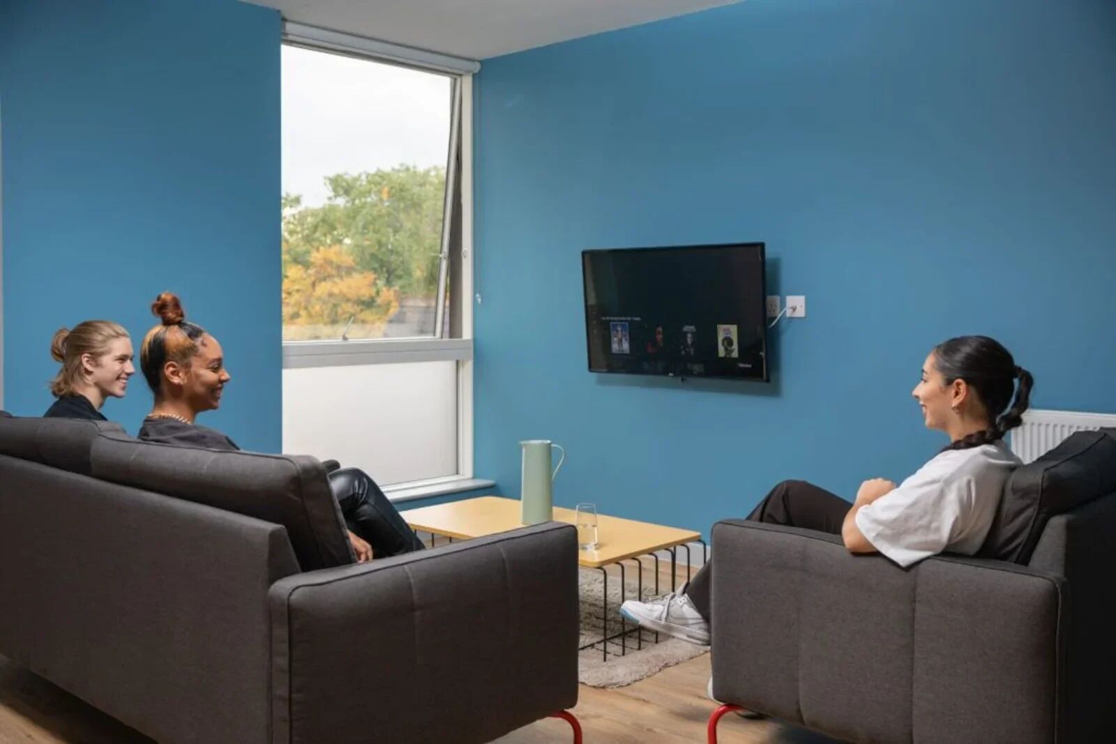 Et moderne værelse med blå vægge, et stort vindue, et fladskærms-tv og to sofaer.