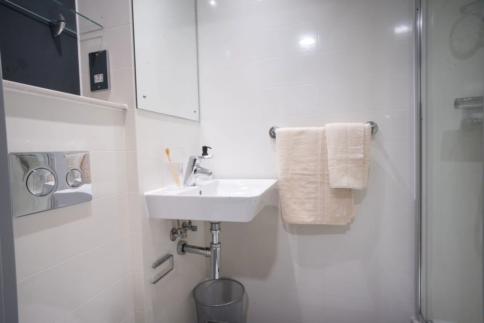 A modern bathroom with a white sink, a glass shower enclosure, and a towel rack.