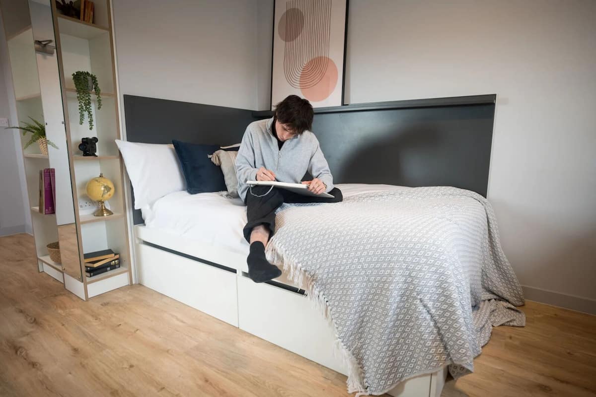 A person sitting on a bed with a globe and books on a shelf beside it.