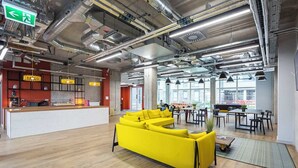 Un espace de bureau moderne avec un canapé jaune vif, un comptoir d’accueil et un coin repas baigné de lumière naturelle.