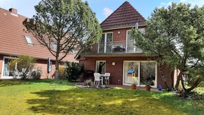 Kaksikerroksinen talo, jossa on parveke, pieni puutarha ja leikkimökki.