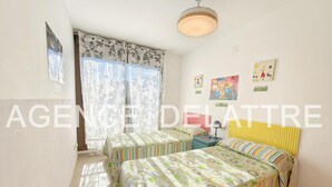 Un dormitorio con dos camas, una ventana con cortinas florales, una lámpara de techo y decoración en la pared.