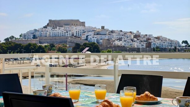 Une table dressée avec des aliments pour le petit-déjeuner, offrant une vue sur une ville côtière aux bâtiments blancs et sur un château.