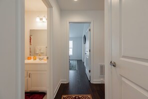 Un pasillo con una puerta blanca a la derecha, otra blanca a la izquierda y un baño con lavamanos y espejo.