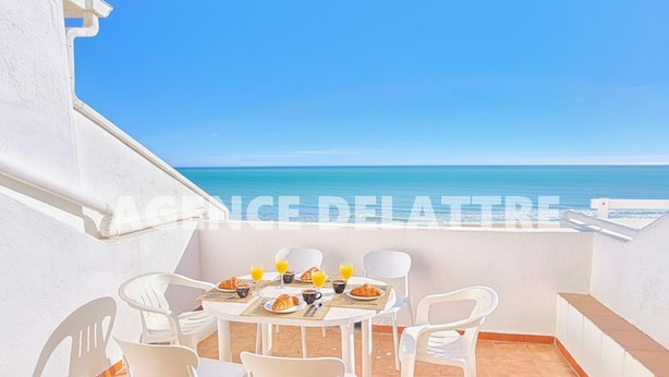 Un balcon avec une table dressée pour le petit-déjeuner, des chaises blanches et une vue sur la mer.