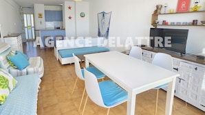 Un salon moderne comprenant un canapé, une table à manger et un téléviseur. Il y a également un coin cuisine avec des placards et un four à micro-ondes.