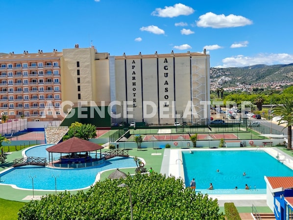 A hotel with multiple swimming pools, a tennis court, and a view of the surrounding landscape.