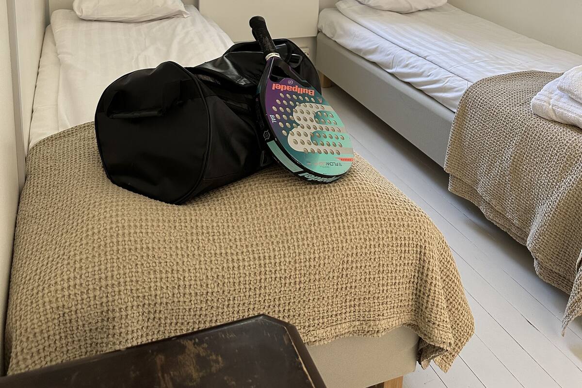 Una habitación con dos camas individuales, una ventana con cortinas, un radiador y una mochila sobre una cama.