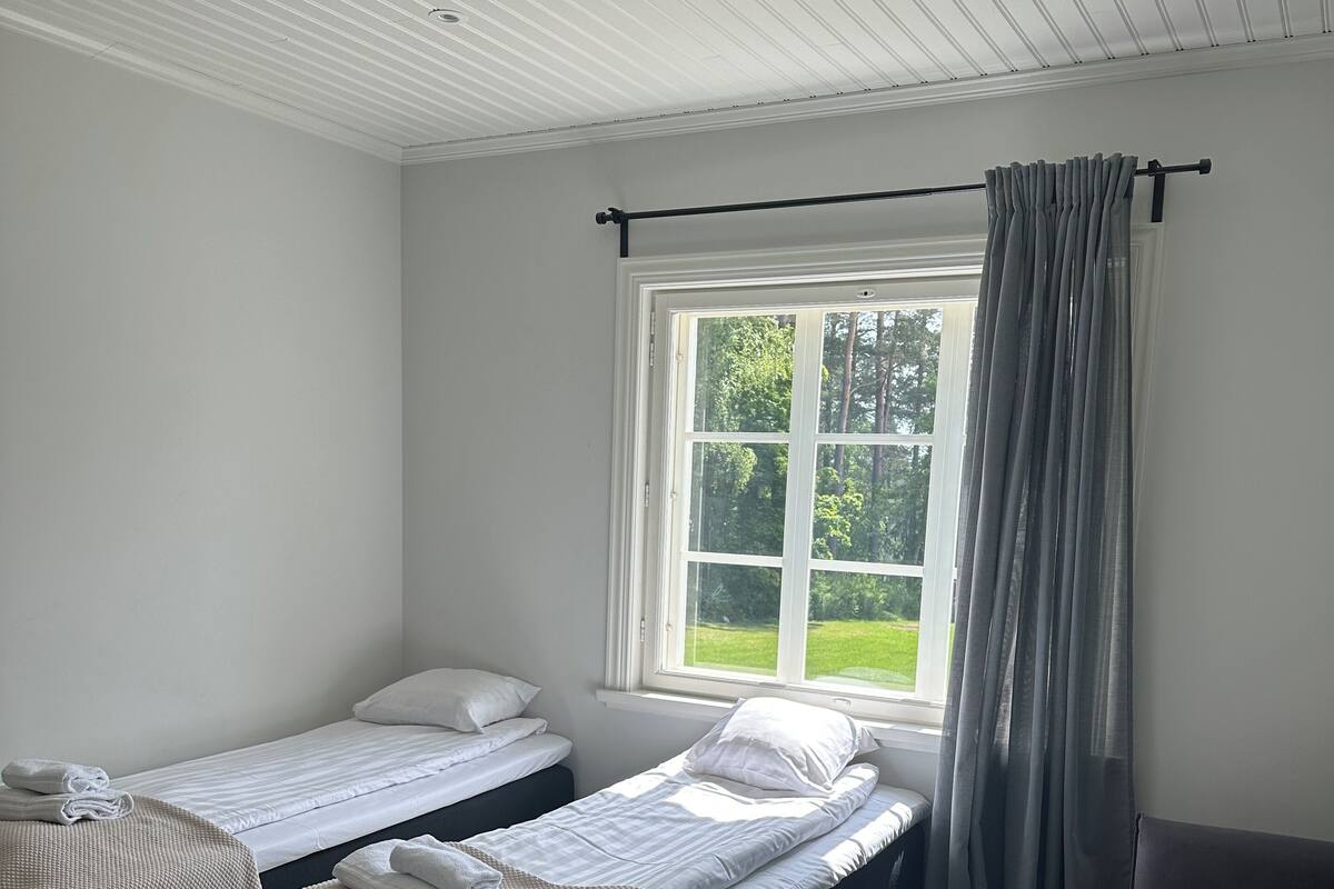 Una habitación con dos camas individuales, un sofá, una ventana con cortinas e iluminación empotrada en el techo.