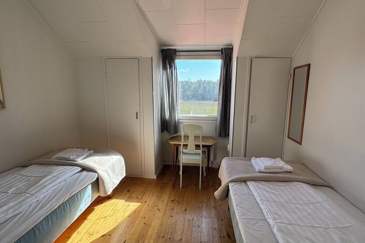 Una habitación con dos camas individuales, una mesita y un ventanal con cortinas.