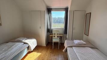 A room with two single beds, a small table, and a window with curtains.