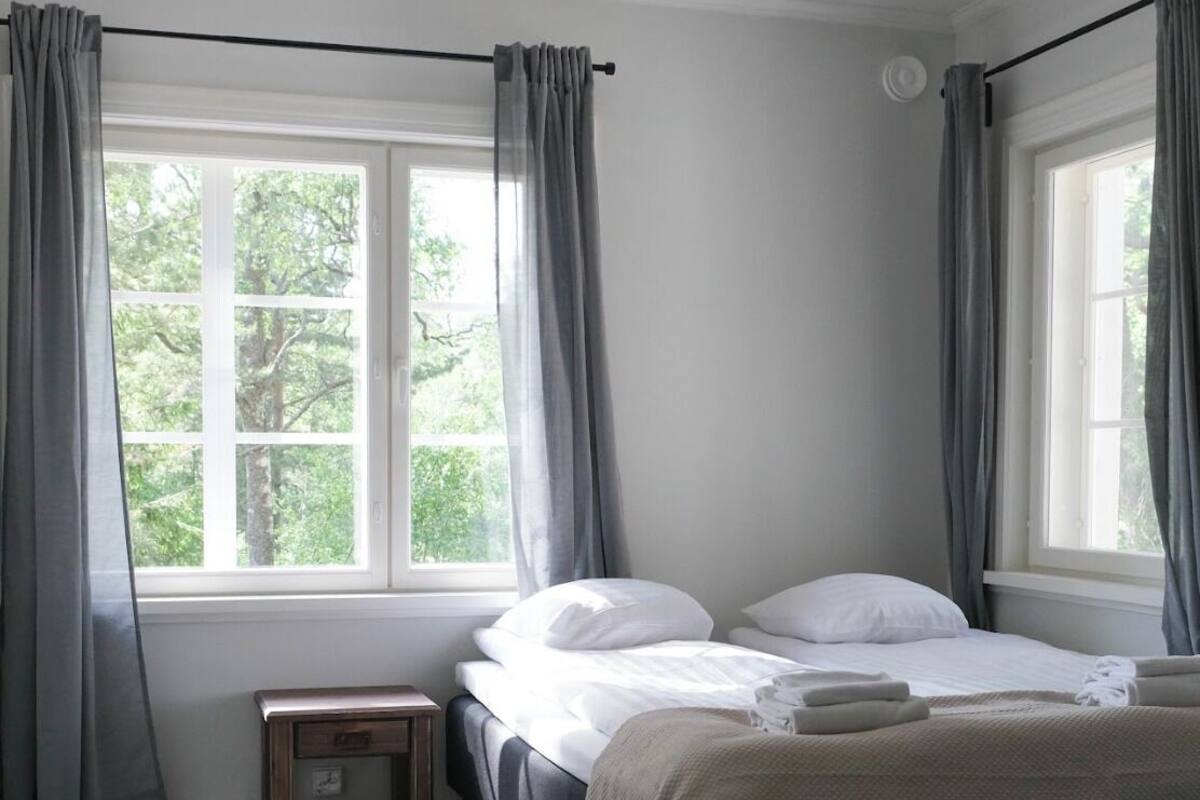 Un dormitorio con cama, mesita de noche y ventana con cortinas.