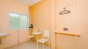 A small, bright room with a white radiator, a window, a sink, two chairs, a small table, and a wall-mounted hanger. - Rockwood house Resort and Thai massage (Phaya Yen)