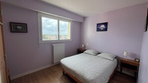Ein Schlafzimmer mit Bett, Fenster, Heizkörper, Nachttisch und einer Wandlampe.