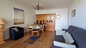 Ein Wohnzimmer mit Sofa, Couchtisch, Esstisch mit Stühlen, Holzschränken und einer Chandelüster.