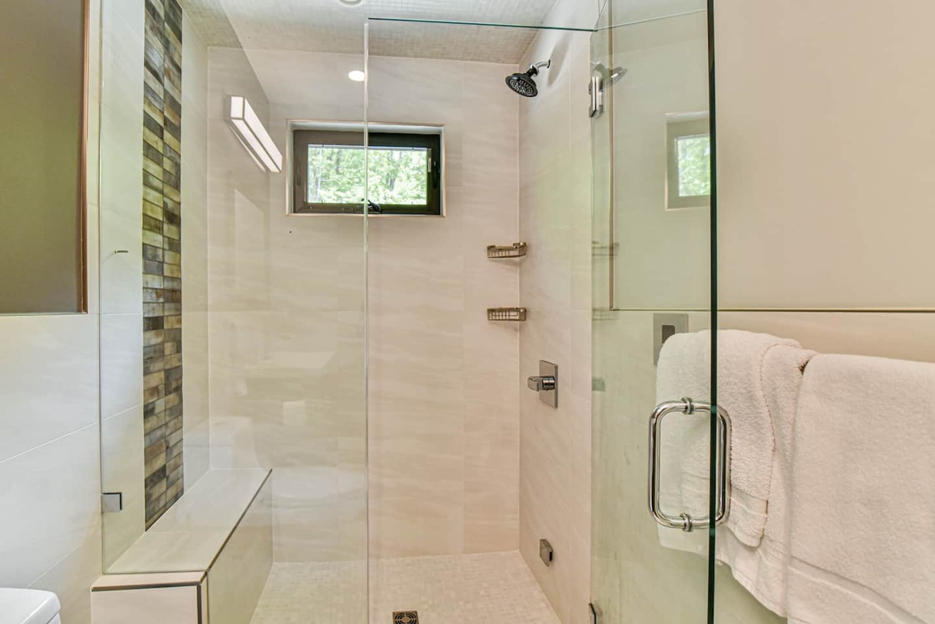 A modern bathroom with a glass-enclosed shower, a small window, and a white towel rack.