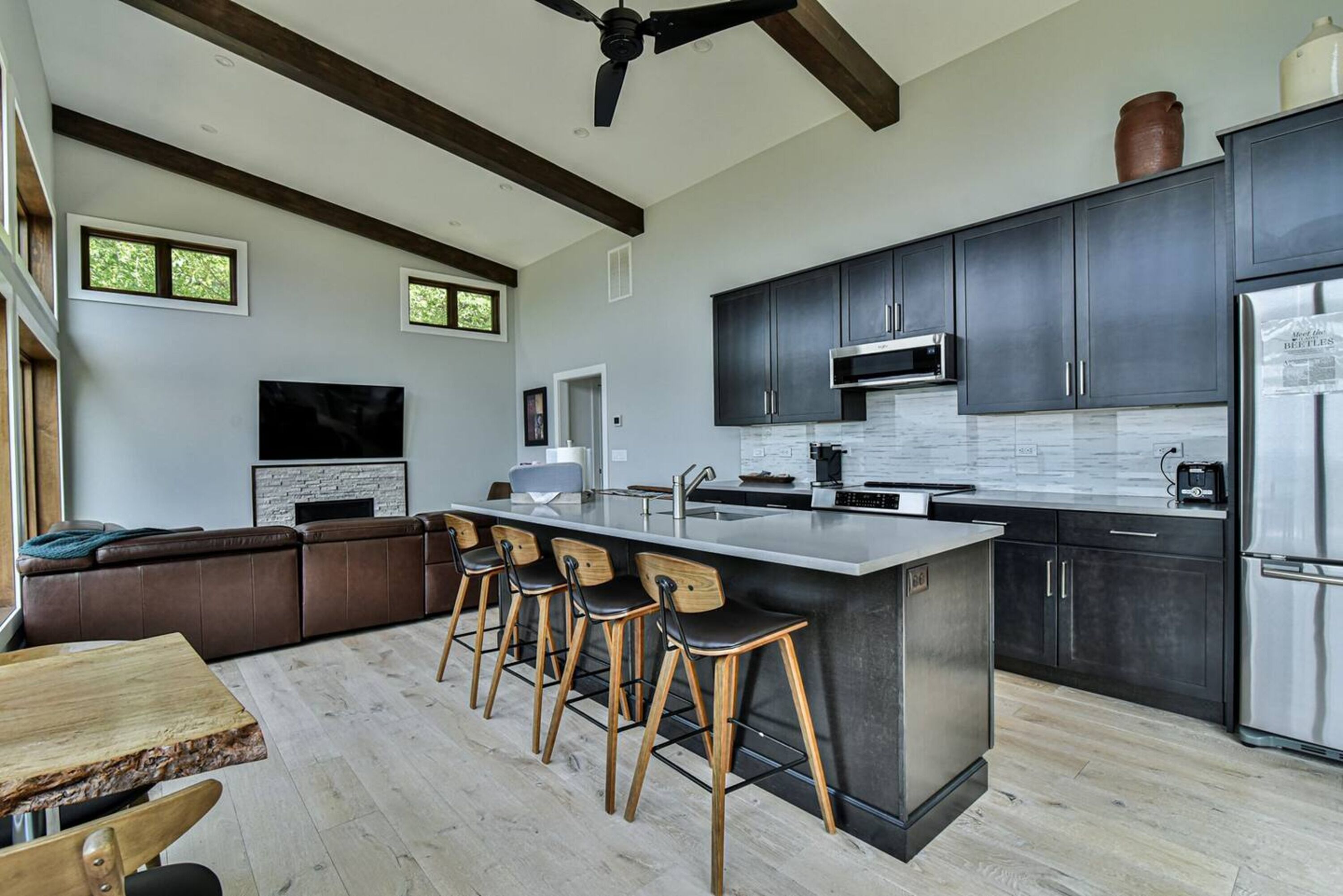 A modern kitchen with dark cabinets, a central island with bar stools, a built-in oven, and a large refrigerator.
