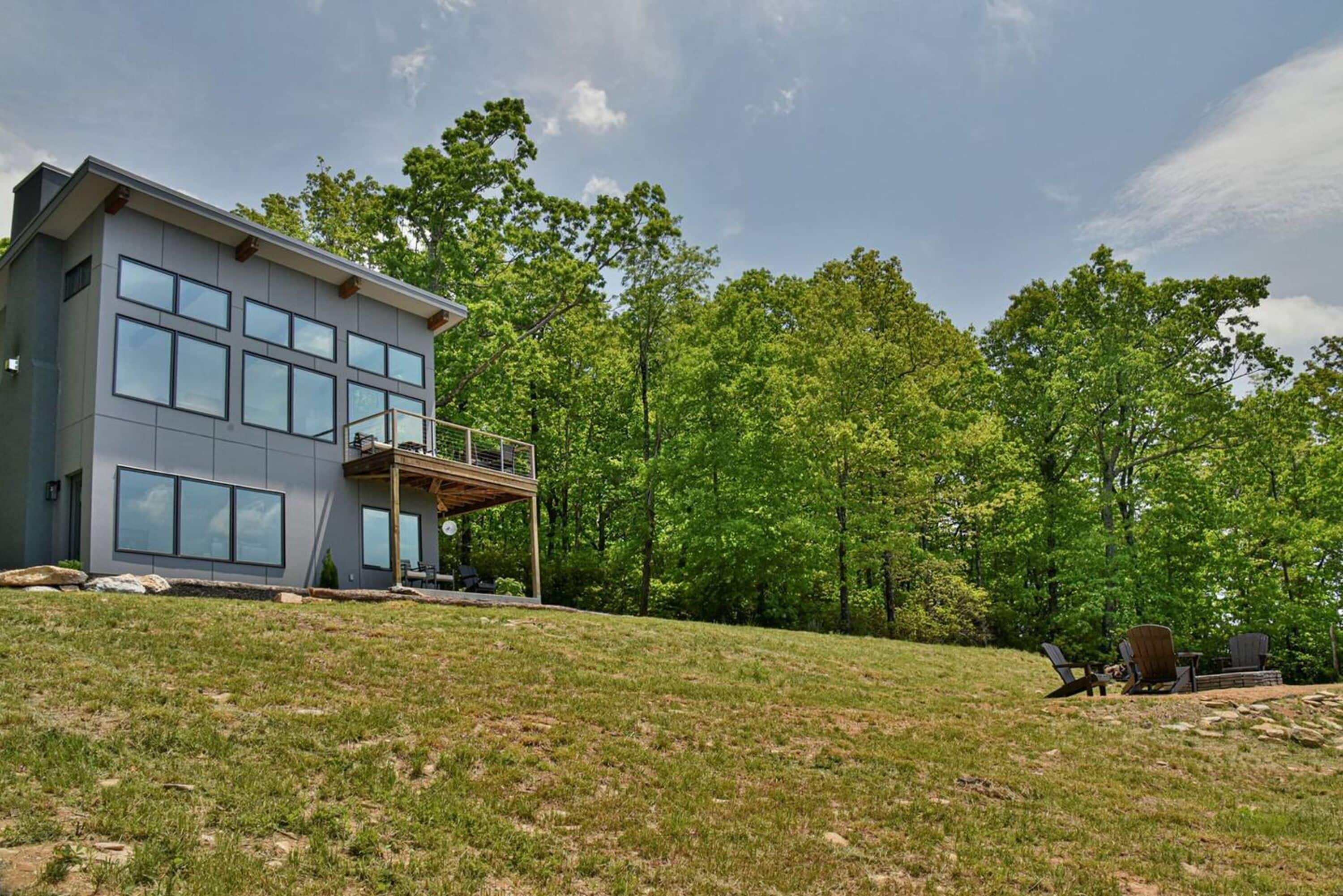 A modern two-story house with large windows, a balcony, and a grassy backyard.