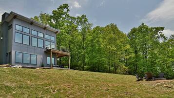 A modern two-story house with large windows, a balcony, and a grassy backyard.