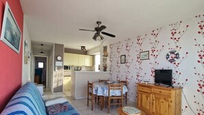 A living room with a sofa, a dining table with chairs, a wooden cabinet, and a ceiling fan.