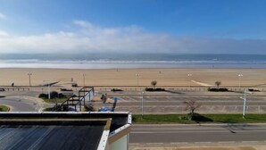 A view of a beach with a parking lot and a road in the foreground.
