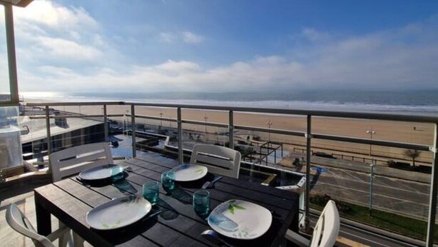 A balcony with a table set for two, overlooking a beach.