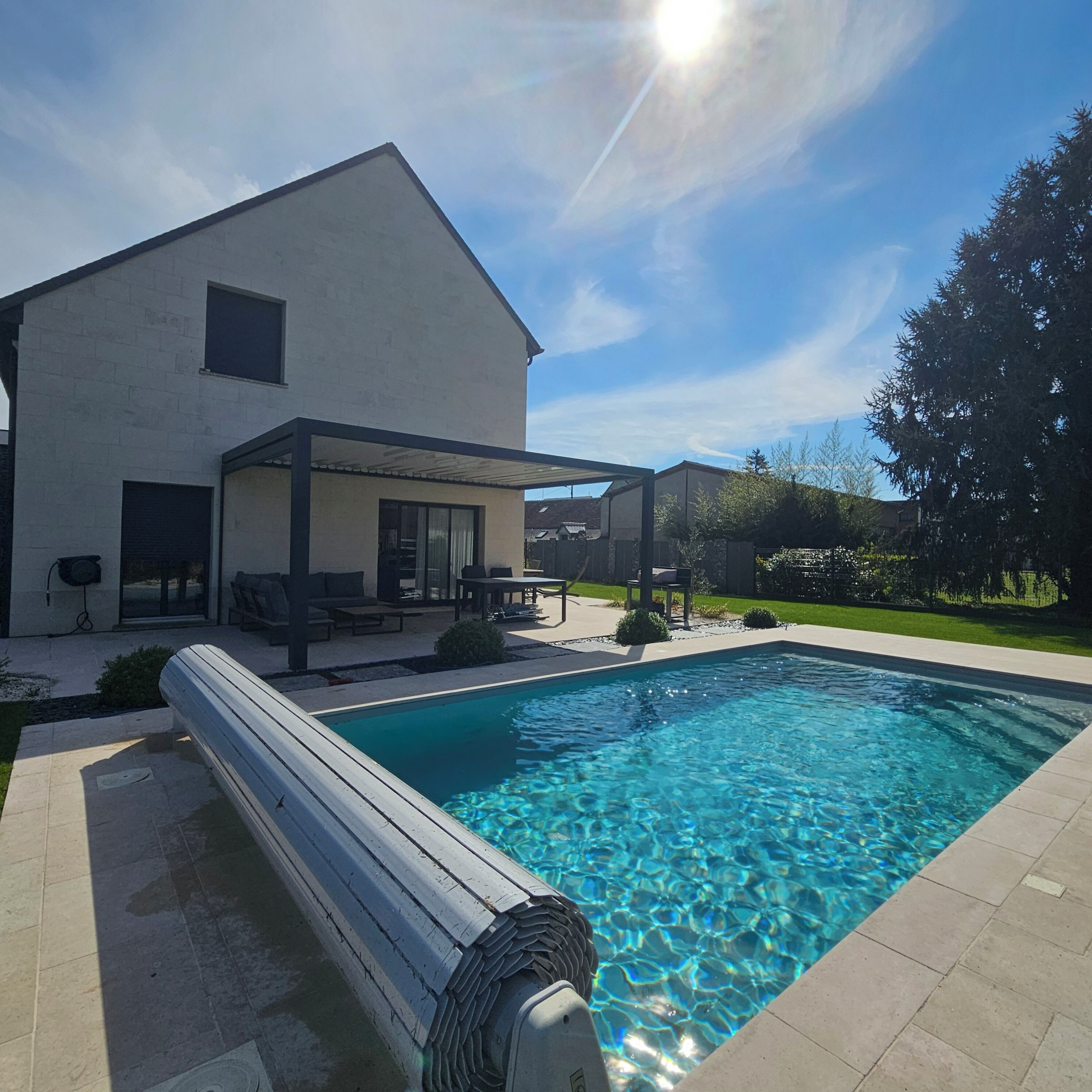 Une maison moderne dotée d’une piscine, d’un espace salon extérieur et d’un patio couvert.