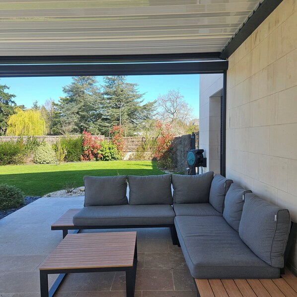 A covered patio with a grey sectional sofa and a wooden table.