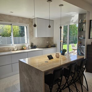 A modern kitchen with a large island, pendant lights, and a view of a garden.