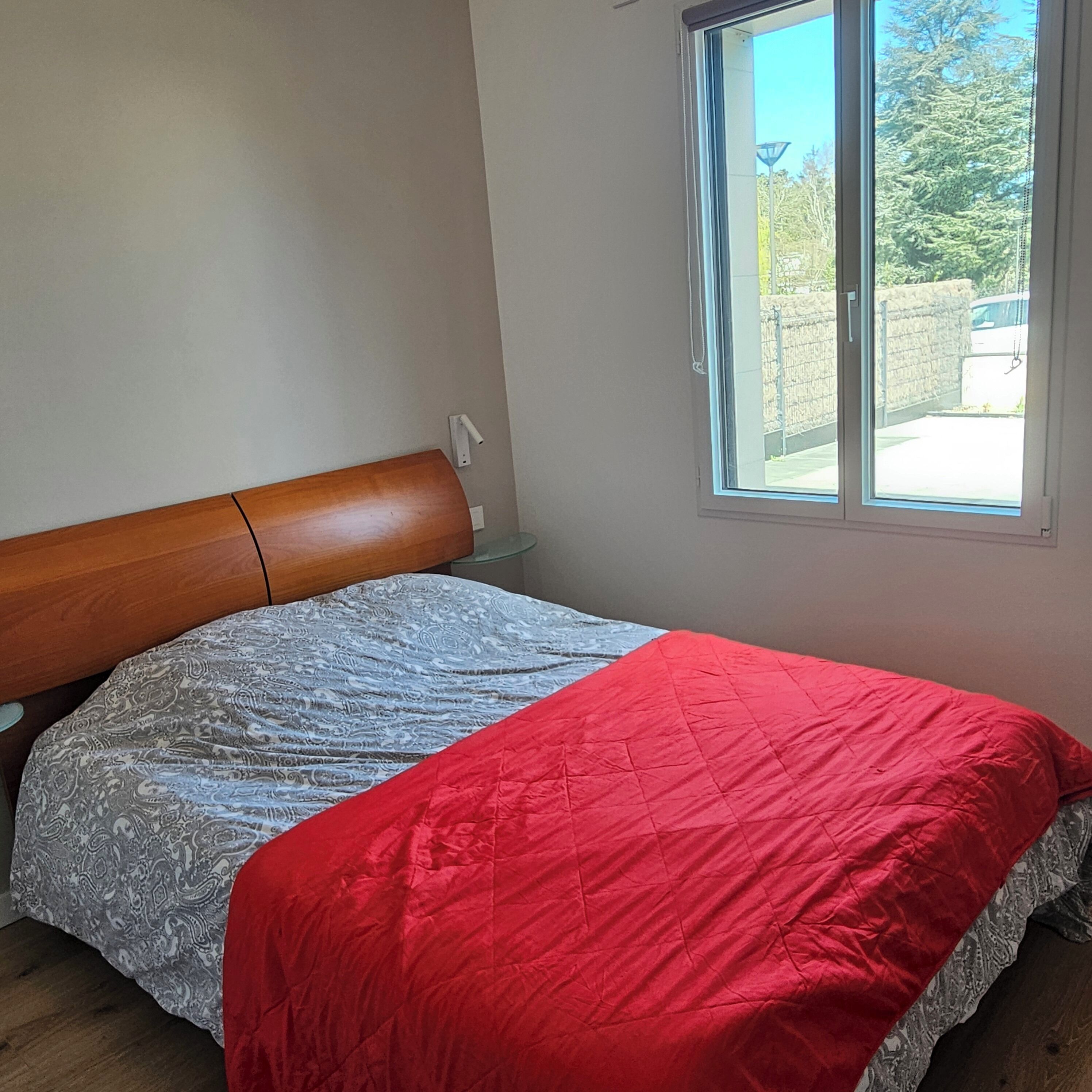 A bedroom with a wooden headboard, a patterned bedspread, and a red quilt.
