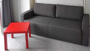 En moderne stue med en grå sofa, et rødt bord og et hvidt skab.